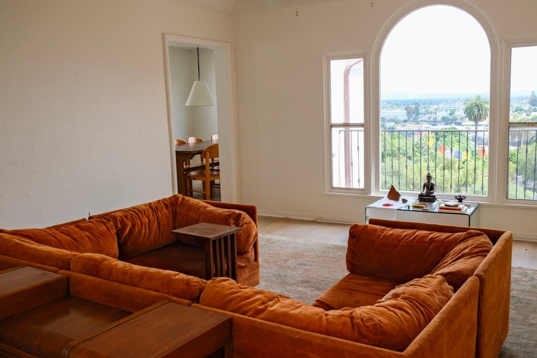 Furnished living room with a rust velvet sectional and a tall arched window overlooking Los Angeles