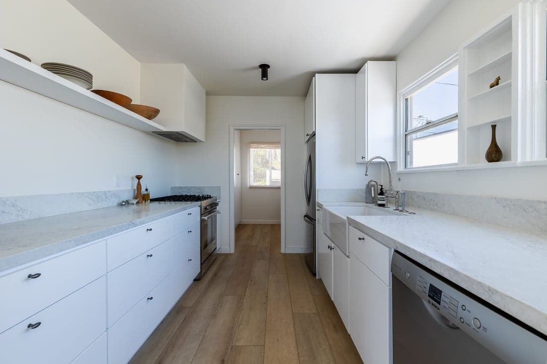 Galley kitchen with white cabinets, stone counters, and wood floors