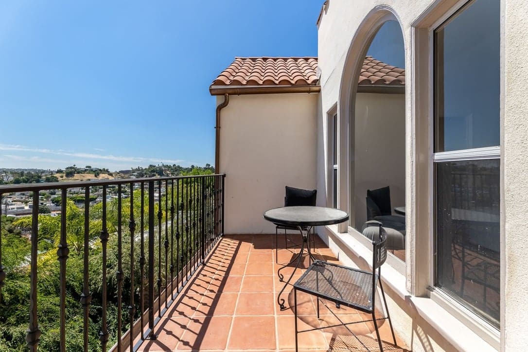 Terracotta-tiled balcony with iron railing overlooking Los Angeles hillside neighborhoods under a blue sky